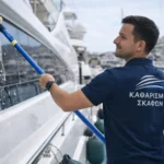 Επαγγελματίας καθαρίζει εξωτερική επιφάνεια yacht με εξοπλισμό σε μαρίνα για υπηρεσίες charter
